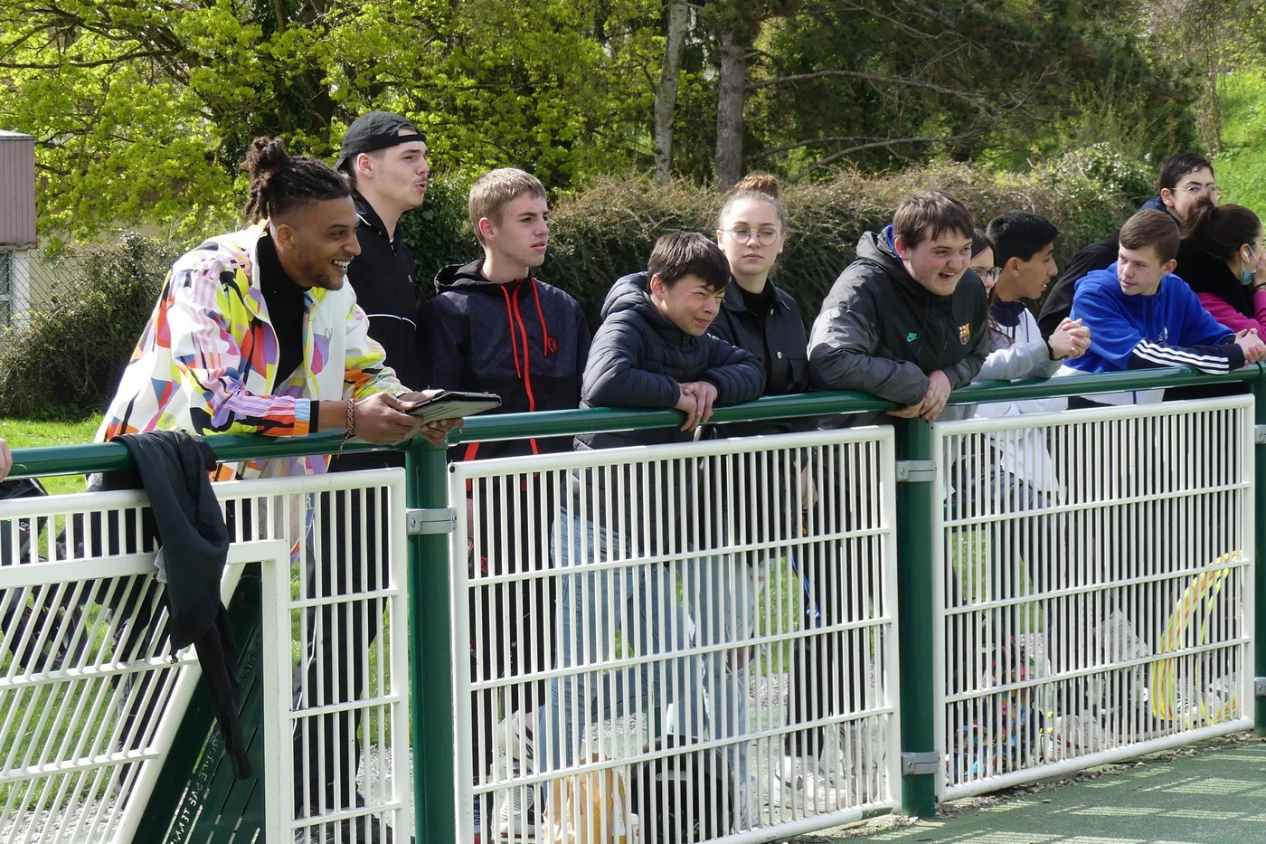 Jeunes joueurs et supporters accoudés à la rambarde d'un city stade, pendant un événement StreetFoot.