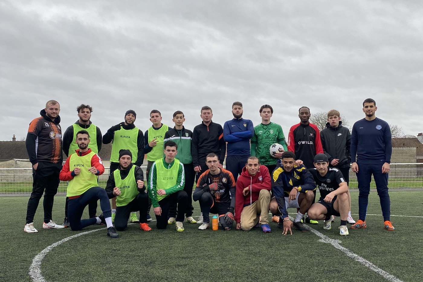 Équipe de joueurs réunie sur un terrain, chasubles et maillots colorés.